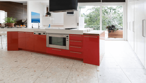 Kitchen interiors made with terrazzo-tycoonstory | tycoonstory media Spacious modern kitchen featuring red cabinetry, built-in appliances, natural light, and elegant terrazzo floor tiles.