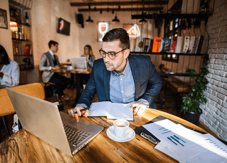 Restaurant marketing ideas Restaurant owner working on a laptop at a café table with marketing reports and coffee, planning effective restaurant marketing ideas to boost visibility, customer engagement, and business growth.