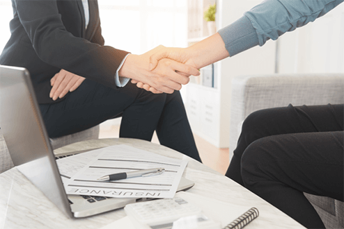 Steps to become an insurance agent-tycoonstory | tycoonstory media A handshake between an insurance agent and a young professional at a conference table, symbolizing a signed agreement on life or business policy coverage.