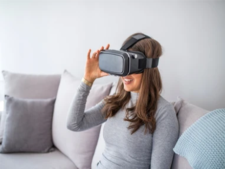 virtual escape room virtual team celebration - tycoonstory | tycoonstory media Woman sitting on a sofa using a vr headset, exploring virtual reality at home.