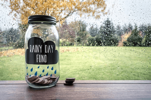 Rainy day fund-tycoonstory | tycoonstory media Rainy day fund jar with coins by a window, representing savings and smart retirement planning for future financial security.