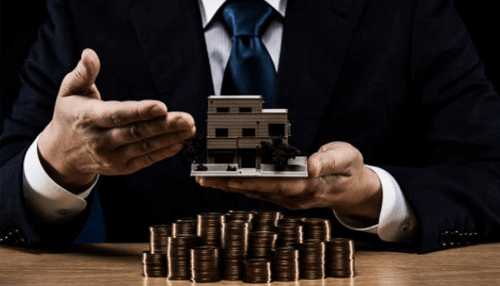 Sell your commercial property A business professional holding a model of commercial property above a pile of coins, symbolizing the value and process to sell your commercial property.