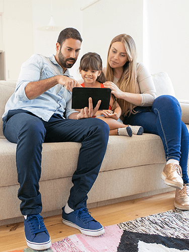 Cheapest electricity provider-tycoonstory | tycoonstory media Happy family sitting on a couch using a digital tablet together in their living room.
