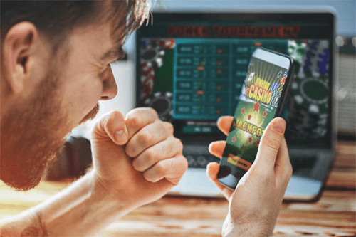 Evaluate real money online casinos-tycoonstory | tycoonstory media A man focused on his smartphone while playing a casino game, showing the excitement of winning at real money online casinos.