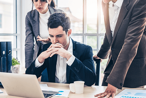 Common business mistakes Business professionals discussing reports around a laptop while looking concerned, illustrating real-world challenges caused by common business mistakes.