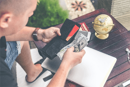 Mode of payment-tycoonstory | tycoonstory media A person holding a wallet with cash and credit cards near a laptop and globe, symbolizing business energy comparison tools.