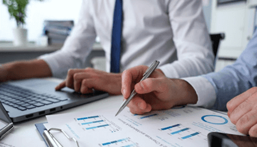 Becoming a franchise Two professionals reviewing charts and data on paper while working on a laptop, representing strategic decision-making and collaboration aimed at business growth.