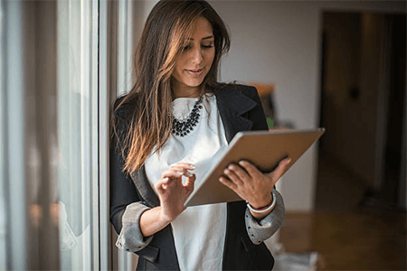 Accessories for business attire Professional woman using a tablet near a window, showcasing modern accessories for business attire that complement a smart business outfit.