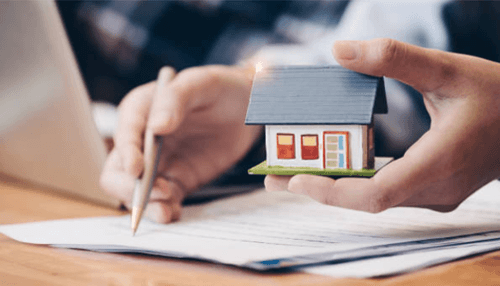 Real estate agent who understands your needs Hand holds a small model house while signing paperwork. Completing the process of buying a home.