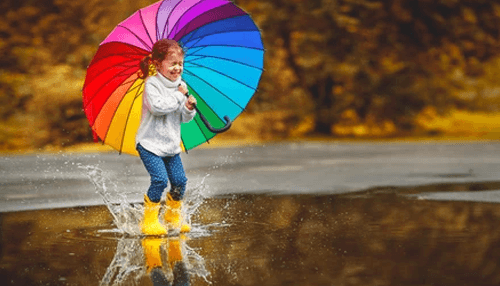 Color options Child playing in a puddle while holding a colorful umbrella on a rainy day.