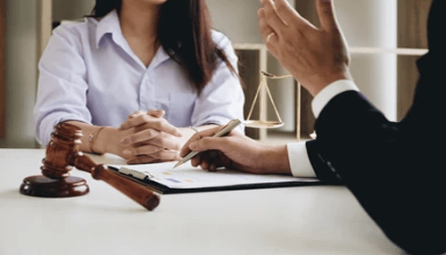 Files lawsuit | tycoonstory media Attorney consulting with a client at a desk with legal documents and scales of justice, illustrating a meeting at a personal injury law firm.