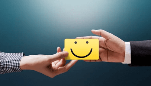Good customer care Two hands exchanging a yellow smiley card, representing customer satisfaction and the positive impact of outsourcing transcription services.