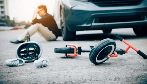 Risks of drunk driving A scene of a drunk driving accident with a small child's tricycle, shoes, and helmet scattered on the pavement in the foreground, and a distraught person sitting near a car in the background