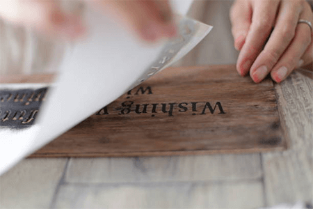 What are the uses of vinyl stencils Vinyl stencils being applied to a wooden sign, showing a hands-on crafting process for custom lettering.
