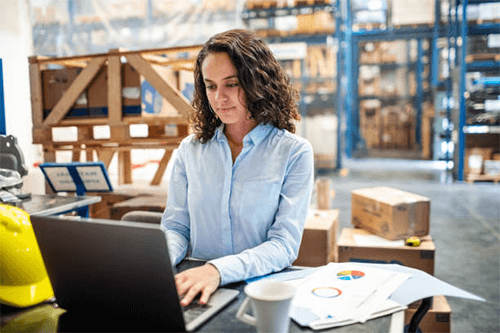 Cargo shipping company extensive experience A woman working on a laptop in a warehouse, analyzing data and planning logistics, symbolizing the modern role of technology in cargo shipping and supply chain management.