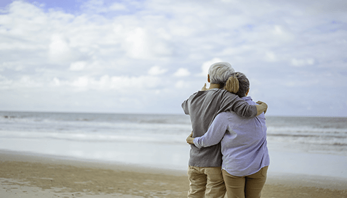 Choosing a retirement plan An elderly couple embracing each other while enjoying a peaceful moment on the beach, symbolizing the rewards of appropriate retirement and long-term planning.