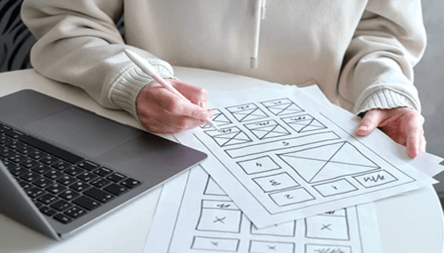 Create a landing page Person sketching a Business Idea layout on paper with a laptop, planning website or project structure.