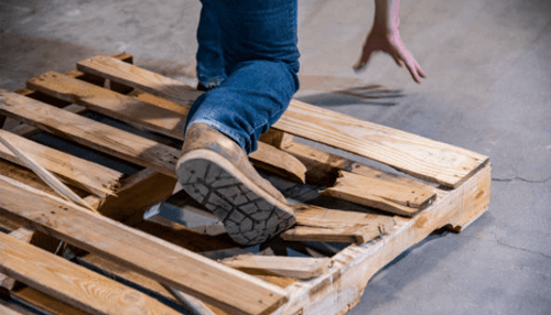 Evidence for the negligence of the third party - tycoonstory | tycoonstory media Worker stepping on a broken wooden pallet, causing a dangerous trip hazard in a warehouse environment.
