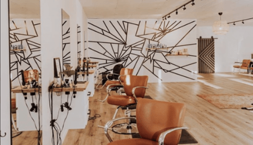 Salon logo Trendy salon interior with geometric wall art, wooden flooring, and organized styling stations.