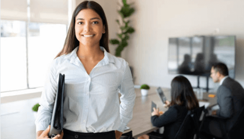 How lawyers help business start-ups Confident businesswoman holding folders in an office with colleagues working in the background, representing professional corporate environment.