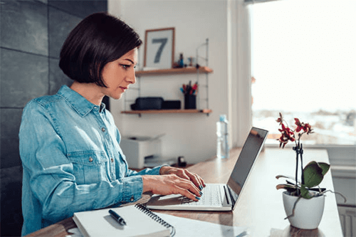 Encourage social interaction A woman working from a home office, focused on her laptop, highlighting the flexibility and productivity of remote team collaboration.