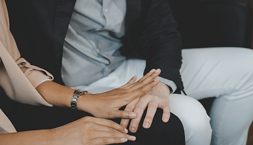 Workplace harassment issue Two individuals sitting together, with one hand reaching out in a gesture that could be indicative of inappropriate behavior in a workplace harassment context.