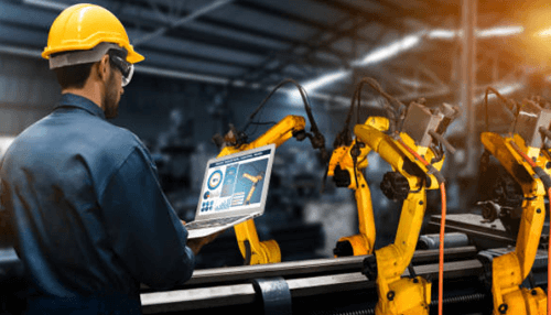 Productive design Worker operating a laptop while overseeing robotic arms in a warehouse, highlighting the integration of automation and technology in warehouse operations.