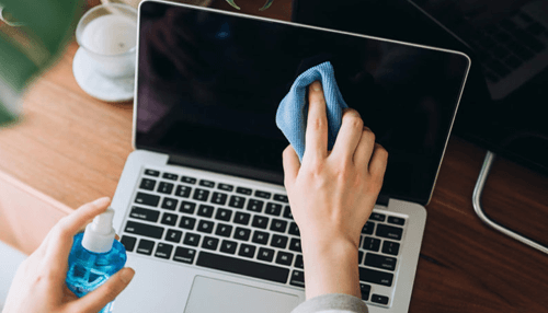 Clean your laptop screen Hand cleaning a laptop screen with a cloth and cleaning solution, demonstrating proper steps to sanitize your laptop effectively.