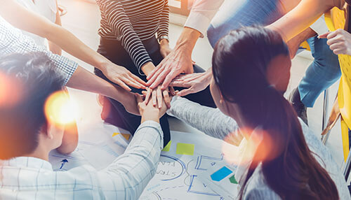 Coordinate with human resources Workplace teamwork with employees joining hands during a collaborative planning session.