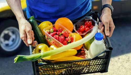 Fresh Fruits and Vegetables Delivery Person holding a crate filled with fresh fruits, vegetables, and dairy items for home delivery service.