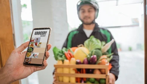 Shop for groceries from the convenience of your own house Shopping for grocery online with mobile ordering and doorstep delivery, illustrated by a grocery delivery person handing over fresh vegetables