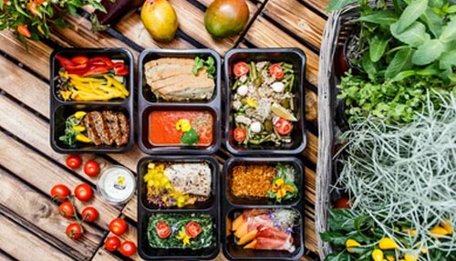 Homemade Food Delivery Healthy meal trays with vegetables and proteins arranged on a wooden table, showcasing ready-to-eat food delivery options.