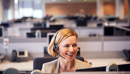 Business phone systems A smiling professional woman wearing a headset in a modern office environment, demonstrating the clarity and efficiency of business phone systems in a customer support setting.