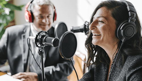 Talk from a script Two professionals recording a business podcasting session with microphones and headphones in a studio setting.