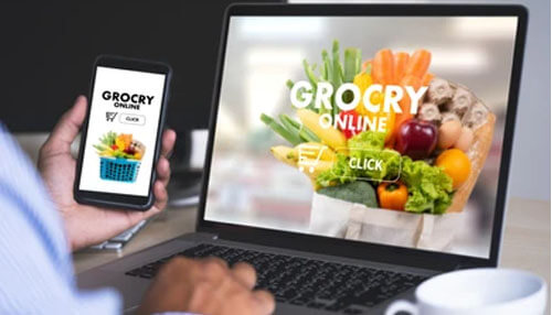 Shopping for grocery online using a laptop and smartphone, showing a digital grocery store with fresh produce displayed on the screen