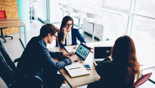 Business budget A diverse team of corporate professionals collaborating over documents and digital growth charts at a large wooden conference table, showcasing the strategic planning required to manage a complex business budget.