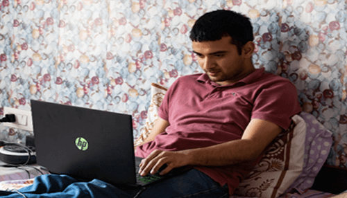 Employees to work remotely - tycoonstory | tycoonstory media A person working on a laptop in a relaxed setting, likely managing personal or business tasks remotely.