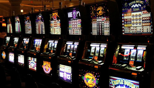 Most popular game styles - tycoonstory | tycoonstory media Slot machines lined up inside a casino, all lit up with various game screens on, showcasing the business of gaming.