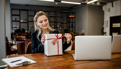 Give a gift Smiling employee in an office opening a gift box, showcasing appreciation and recognition in the workplace.