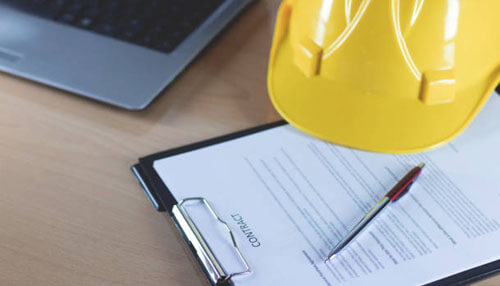How to get a contract template A design contract on a clipboard with a pen and yellow hard hat placed on top, symbolizing the signing of contracts for construction projects, supported by bonsai's templates