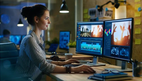 Take your editing to the next level A woman editing content on dual monitors, representing the work involved in creating engaging content to get your instagram profile noticed