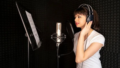 Make it easy to say A woman recording voiceover scripts in a professional sound booth with headphones, preparing for voice work