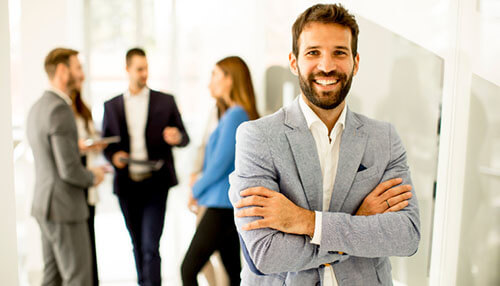 Confident businessman standing in front of colleagues discussing in the background, representing leadership and diversity and inclusion in a workplace. Diversity and inclusion in the workplace