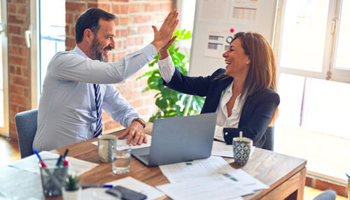 Elijah norton lists 8 ways to help run a successful business - tycoonstory | tycoonstory media Two colleagues high-fiving in celebration, representing a successful business achievement and teamwork.