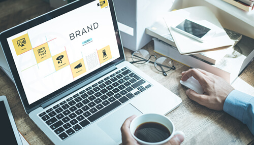 Promotion of the brand image - tycoonstory | tycoonstory media Infographics branding strategy displayed on laptop screen with design layout, coffee cup, and workspace setup.