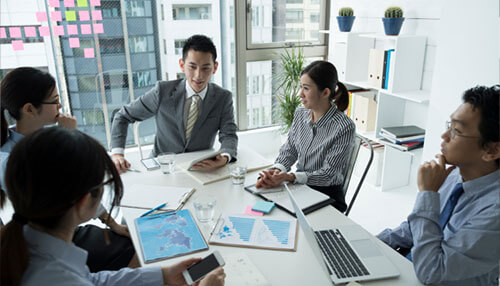 Benefits of company incorporation in hong kong - tycoonstory | tycoonstory media Business offshore strategy meeting in a modern office environment, showing a diverse team discussing plans, charts, and maps.