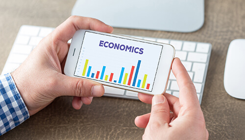 Economics Study business and management: a person holding a smartphone displaying a bar chart with economics.