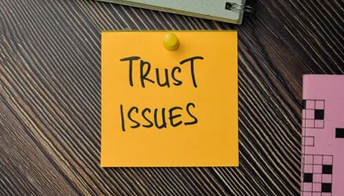 Trust issues - tycoonstory | tycoonstory media A yellow sticky note pinned on a wooden surface with words on it: trust issues, pointing towards team management problems and solutions.