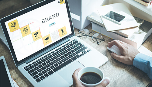 Use visuals to promote your brand A person using a laptop to design a brand strategy, showing an ecommerce dashboard with icons for website management, digital advertising, and online marketing analytics.