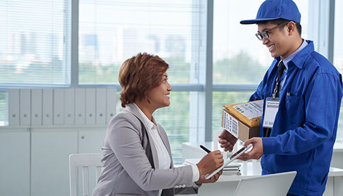 How to negotiate the best rates for bulk mailing A postal worker delivering a package to a woman in an office, demonstrating the logistics and service involved in bulk mail outsourcing.